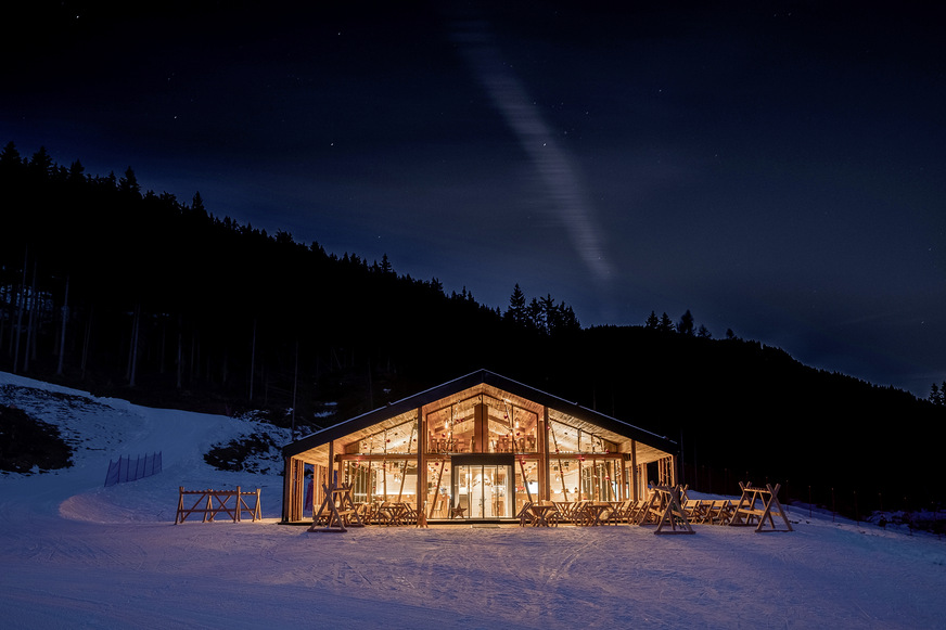 Bei Dunkelheit laden die vollverglasten Fenster- und Fassadenflächen die Skifahrer und Wanderer zur Einkehr in das heimelige Chalet ein.