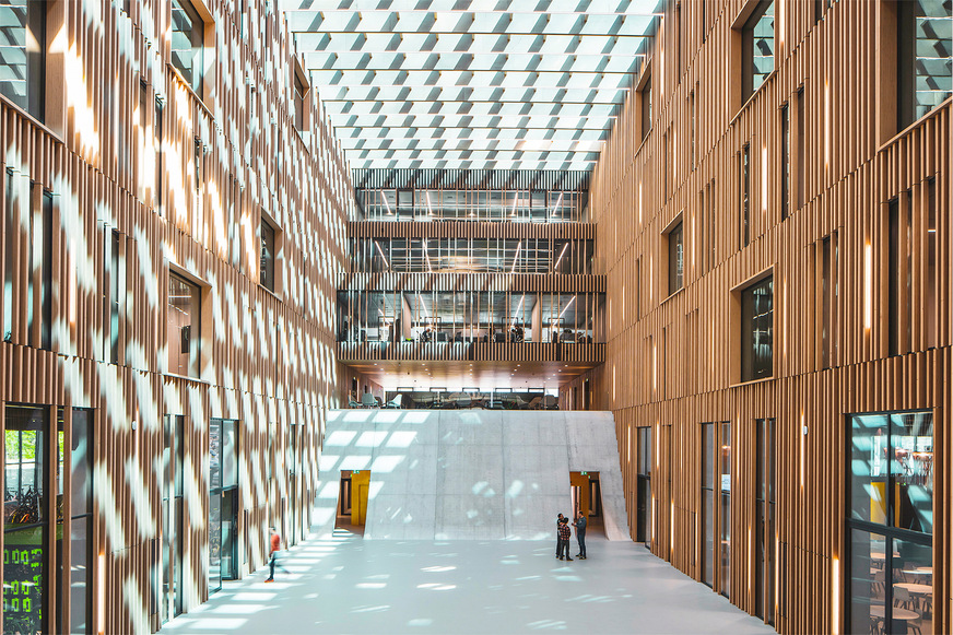 Spannende Licht- und Schattenspiele im Atrium werden durch das einfallende Tageslicht und die strukturierten Holzlamellen erzeugt.