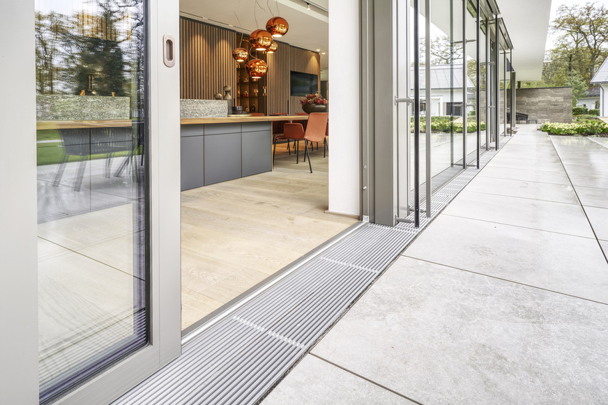 Das edle Design des Gitter­rosts ist technisch ausgereift: Die Design­gleichheit von Boden­schwelle und Ent­wässerungsrinne sorgt für ­eine nahtlose, einheitliche Optik über die ­komplette Fensterfront des ­Gebäudes hinweg.