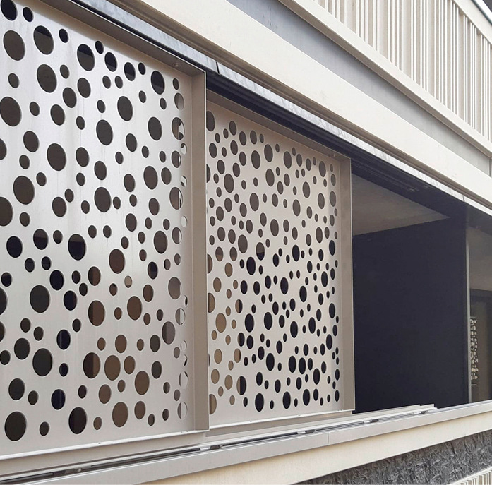Schiebeläden mit Lochblech bilden den Abschluss eines Balkongeländers in einem großen Wohnhaus.