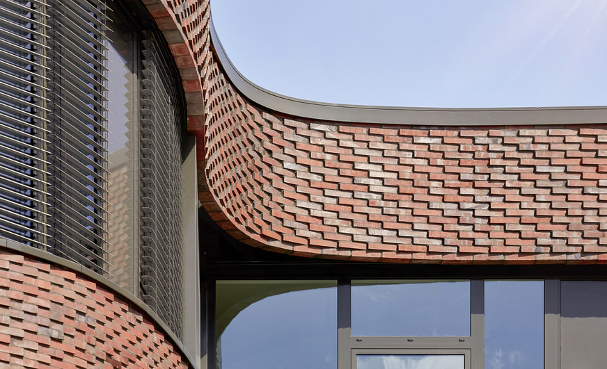 Eine technisch ausgefeilte Fassadenkonstruktion verwandelt in den ­abgerundeten Gebäudeecken auch die umlaufenden Fenster- und ­Brüstungsbänder in fließende Kurven.