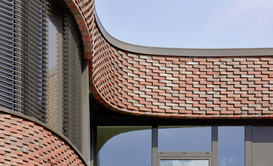 Eine technisch ausgefeilte Fassadenkonstruktion verwandelt in den abgerundeten Gebäudeecken auch die umlaufenden Fenster- und Brüstungsbänder in fließende Kurven.