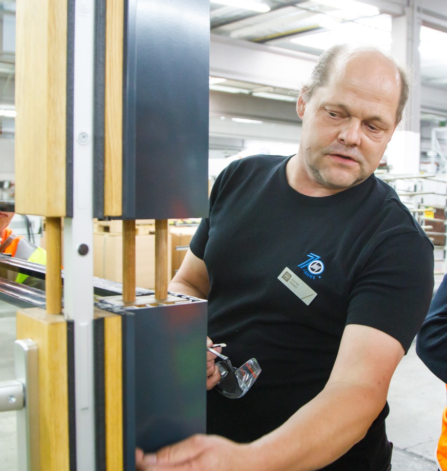 Günter Haseitl im Austausch mit Kunden am Muster der Hebe-Schiebe-Türe im Manufakturbereich für Holz-Aluminium-Rahmen.