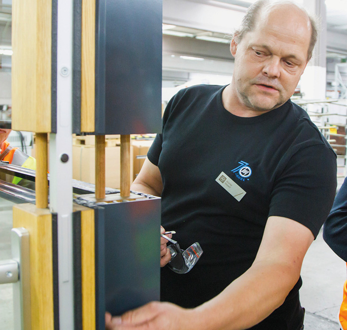 Günter Haseitl im Austausch mit Kunden am Muster der Hebe-Schiebe-Tür im Manufakturbereich für Holz-Aluminium-Rahmen