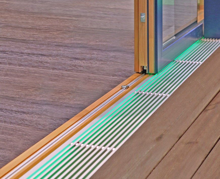 Die Nullbarriere-Schwelle, bei der die Laufschiene in das Bodenprofil eingelassen ist, schafft einen eleganten, bodenbündigen Übergang. Eine integrierte Lichtleiste sorgt für stimmungsvolle Akzente im Raum.