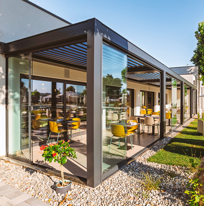 Rahmenlose Line-Glass-Verglasungen, Vertika-Prime-Senkrechtmarkisen und integrierte LED-Lichtbänder schaffen einen flexibel nutzbaren Gastronomiebereich.