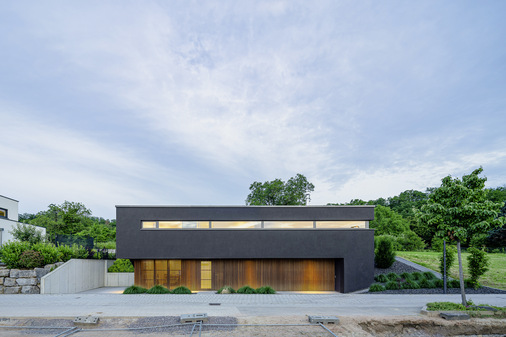 Das Einfamilienhaus in Hang- und Feldrandlage wirkt zur Straße hin zugeknöpft und kompakt. Zur Gartenseite hin öffnet sich die Fassade mit großzügigen Glasflächen. 