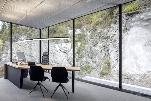 Die Büros im Obergeschoss blicken auf die steinige Felswand und die bewaldeten ­Hügel der Umgebung. Die Nutzer haben das Gefühl, direkt in der Landschaft zu sitzen. - © Foto: m2 Railgroup – Pederoa
