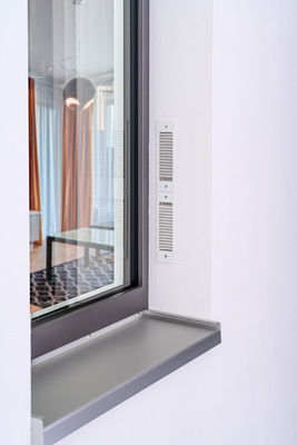 Das Zwei-Wege-Lüftungsgerät „Caire smart“ wird ins Fenstersystem integriert (seitlich oder oben, mit sichtbarem, farblich angepasstem Gehäuseprofil) und kann überdämmt und überputzt werden.