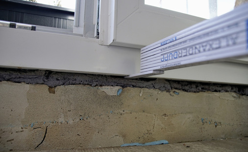 Unterer Anschluss eines Fensterrahmens auf einen Mauersockel. 
Nach Abnehmen des PVC-Deckbrettes ist lediglich Polyurethan-Ortschaum ­festzustellen. Der innere Anschluss fehlt komplett.