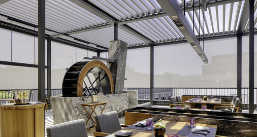 Bei senkrecht gestellten Lamellen setzt das Licht- und Schattenspiel den zentral liegenden Brunnen besonders wirkungsvoll in Szene.