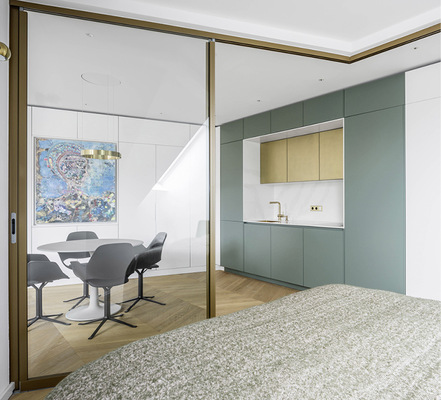 Der helle Schlafraum wirkt großzügig und schafft Blick auf den Eyecatcher der Wohnung: Die farbige Küchenzeile.