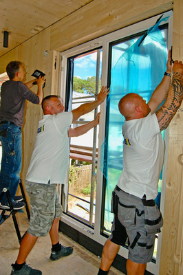 Drin das Ding: Monteure, Anwendungstechniker, Sachverständiger – beim Einsetzen des Holz-Aluminium Elements packen alle mit an. Wie immer wird zunächst oben eingefädelt, erst dann das Element mit der Festverglasung unten auf den Sockelpunkt des auf null gesetzten Vorwandmontage-Profils gestellt.