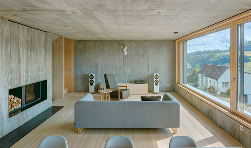 Der offene Wohn-Essbereich und die Küche werden dank grossen Fensterfronten zur Straße und zum Hang mit viel Tageslicht durchflutet.