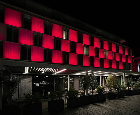 Das beleuchtete Farbenspiel an Fassade und Lamellendächern spiegelt in der Nacht das besondere Ambiente des Hotels wider.
