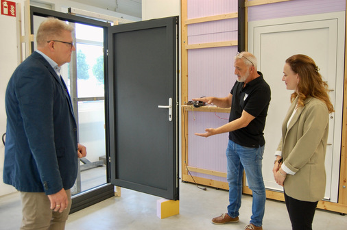 Leiter Produktmanagement Thomas Ochsenreither von der Groke Türen GmbH mit Marcus Müller (li.), Leitung Vertrieb, und Verena Schilling, Vertriebsassistenz, von der Gargiulo GmbH an der Klimakammer des Herstellers von Aluminium Hauseingangstüren. An der Haustüre links ist unten das zugelieferte Unterbauprofil INSUFOX aus hoch wärmedämmendem PET-Schaum erkennbar.