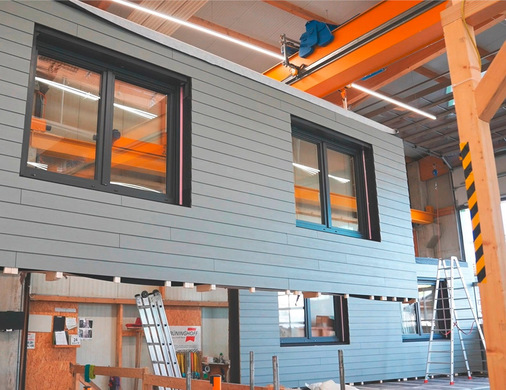 Die Fassadenelemente werden in der Werkshalle vollständig vormontiert, mit integrierten Fenstern, Dämmung und Versorgungstechnik.