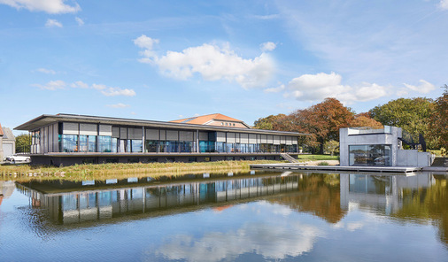 Das Gebäude scheint über dem Wasser zu schweben, während der halb geöffnete Metallbehang s_enro der Fassade eine leichte, changierende Tiefe verleiht.