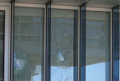 (2) Zerstörtes Floatglas und beschädigtes VSG im Innenbereich. Einfaches Floatglas reicht nicht aus, um weitere Schäden zu verhindern. Bei diesem Fassadenaufbau wäre das Anbringen von Prallscheiben ohne größere optische Beeinträchtigungen möglich. Bruchbild: Unregelmäßige Einwurfstelle, große, unregelmäßige und spitze Scherben