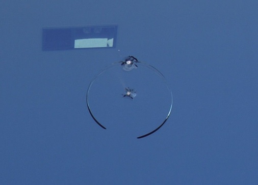 (5) VSG aus 2 x 10mm Float als Absturz sichernde Verglasung. Tatwerkzeug: Steinwurf oder Wurfkörper aus Metall. Bruchbild: In der Mitte unregelmäßiger Kegel, der nur die äußere Scheibe beschädigt, dazu ein nicht geschlossener kreisrunder Bruch (4) Wird ESG zerstört, bilden sich große Schollen, hier durch Reflexionsänderungen erkennbar, die erst beim Aufprall am Boden in unzählige kleine stumpfwinkelige Bruchstücke zerspringen