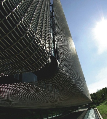 Als äußere Haut wurde GKD-Gewebe vom Typ Omega 1847 aus Edelstahl und eloxiertem Aluminium, schräg vor die Glasfassade gespannt und oben und unten je um 90 Grad umgelenkt.