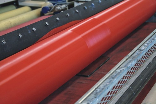 Farbauftrag im Walzenverfahren (Rollercoat)Die Glasplatte, die Riccardo Booz im Bild links in Händen hält, wird hier mittels Walze bedruckt. Gut zu sehen ist Farbe oberhalb der Walze, die sich nach und nach über die ganze Walze verteilt.