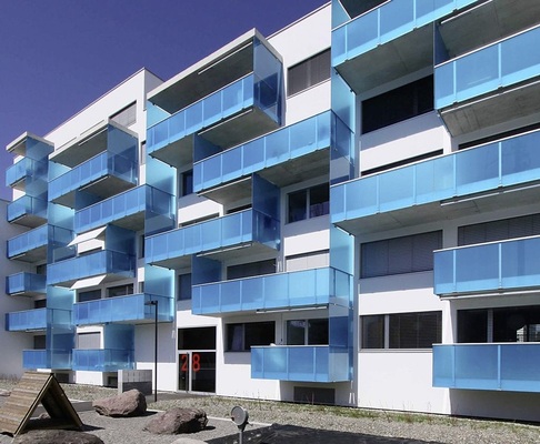 Balkone mit VSG und blauer trans­luzenter FolieDie Balkone sind mit Brüstungen (VSG 2x12 mm) mit blauer Verbund­folie ­ausgerüstet, die gegen die ­weiße ­Fassade kontrastiert und südländische ­Stimmung ver­mitteln soll.