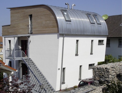 Strandkorb: Zweifamilienhaus auf schmalem Grundstück. Das Blechdach überspannt das gesamte Dachgeschoss (Fensterbauer: Wiegand Fensterbau).