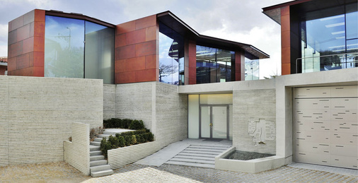 Die drei getrennten Baukörper thronen auf einem Sockel aus Mauerwerk, fließen aber im Untergeschoss zu einer Ebene ineinander. Die großzügigen, raumhohen Isolierverglasungen sind Bestandteil der Konstruktion und sowohl transparent als transluzent gestaltet.