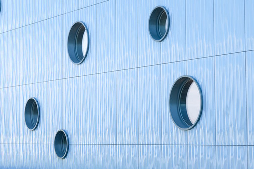 Kreisrunde Fenster aus GENEO Profilen setzen in der blauen Wellenfassade ansprechende Designakzente.