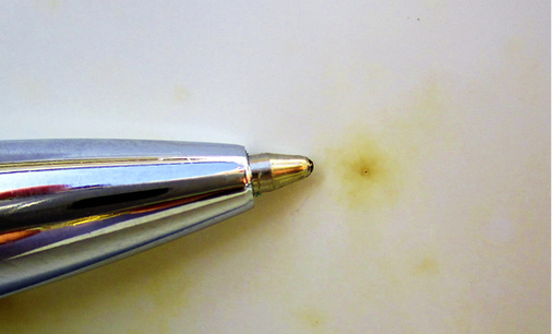 



Oxidierender Metallspan von einem gelben Hof umgeben; zum Größenvergleich links daneben eine Kugelschreiberspitze.
