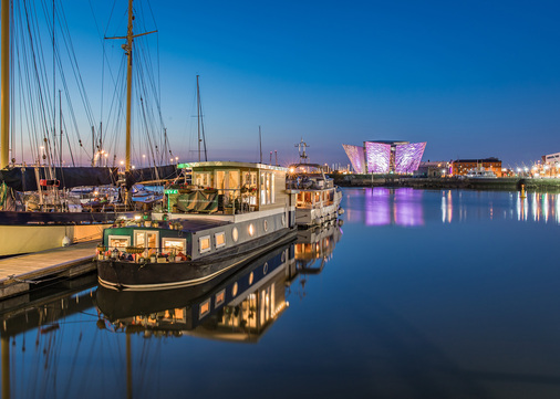 Nachts fällt der Blick durch die großen Fenster auf das spektakulär erleuchtete Schifffahrtsmuseum “Titanic Belfast“.