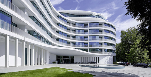 



Bei dem Neubau wickeln sich horizontale Bänder aus Glas und schneeweiß glasierte großformatige Keramikplatten wie an einem endlos wirkenden Band um das Gebäude. 
