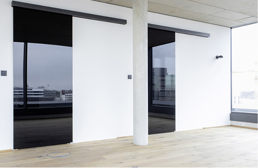 



Automatische Schiebetüren aus schwarz durchgefärbtem ESG markieren den Zugang zu den Sanitärbereichen des neuen Verwaltungsbaus in Bremen. 
