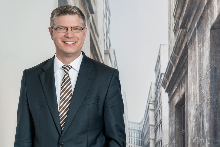 Lächelnder Mann im Anzug und mit gestreifter Krawatte vor einer Stadtlandschaft im Hintergrund. - © Leinemann Partner Rechtsanwälte