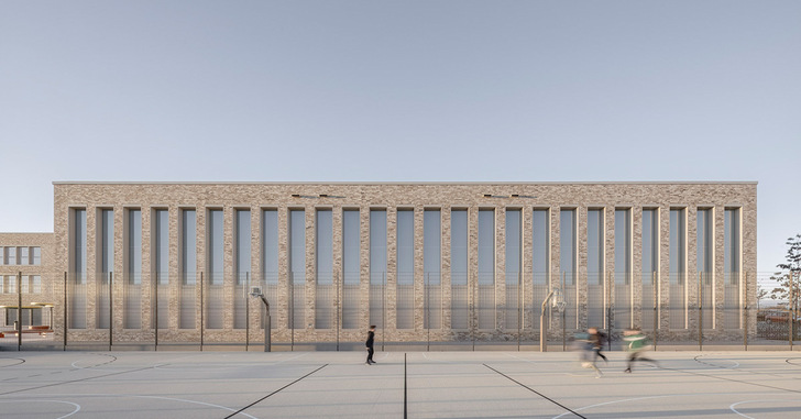 Modernes Backsteingebäude mit hohen vertikalen Fenstern, gesehen von einem leeren Sportplatz im Freien, auf dem ein paar Leute herumlaufen. - © Markus Guhl, Architektur: mvm+starke