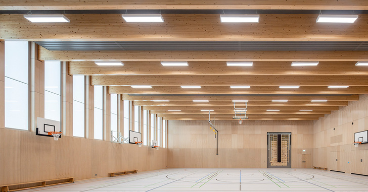 Geräumige, moderne Sporthalle mit Holzbalken, Basketballkörben und Spielfeldmarkierungen. - © Markus Guhl, Architektur: mvm+starke
