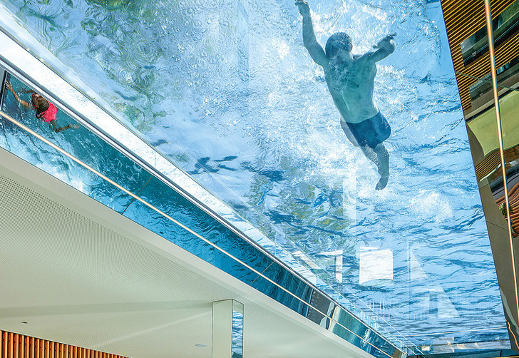 32 m of ceiling made from glass and water: the transparent bottom of the pool provides a special swimming experience and the water creates unique light effects in the interior of the building