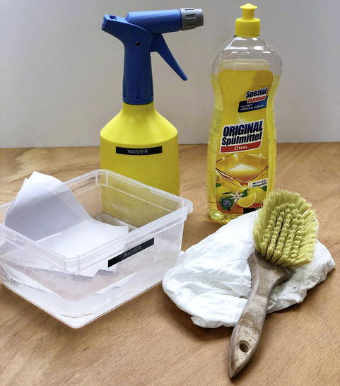 Das passende Equipment, um Folienoberflächen von Verschmutzungen zu befreien: Sprühflasche mit heißem Wasser, Spülmittel, weißes Papier, ein weicher Lappen und eine weiche Bürste.