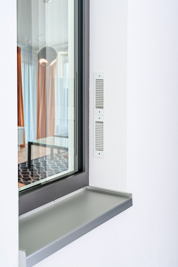 Das Zwei-Wege-Lüftungsgerät „Caire smart“ wird ins Fenstersystem integriert (seitlich oder oben, mit sichtbarem, farblich angepasstem Gehäuseprofil) und kann überdämmt und überputzt werden. - © Foto: Gealan
