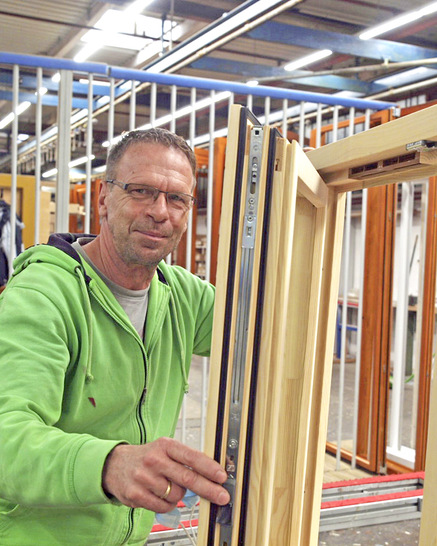 Joachim Kleinert präsentiert ein fertig zusammengesetztes Holzfenster mit Fensterfalzlüftern von Regel-air.