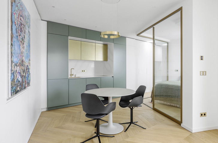 Die Küchenzeile in grünen und goldenen Farbtönen grenzt sich optisch zum Wohnzimmer und Schlafbereich ab.