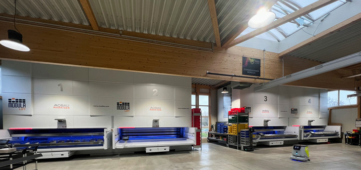 Das 4-fache Modula Lift System kann bis zu 180.000 kg lagern, und arbeitet nach dem „Ware zum Mann“-Prinzip. Im Vordergrund reinigt Pudu CC1 die Bodenfläche.