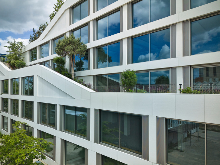 Raumhohe Pfosten-Riegel-Konstruktionen mit schmalen Profilansichten werden von schmalen Lüftungsflügeln flankiert.