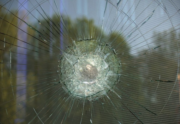 (1) Detailaufnahme eines Angriffs mit einem Steinwurf, Wurfkörpern aus Metall oder Brech­eisen auf VSG aus 2 x 4mm Floatglas. Deutlich ist die Wirkung der Verbindungsschicht aus Polyvinylbutyral (PVB) mit einer Stärke von 0,38mm zu sehen, die nicht durchdrungen wird