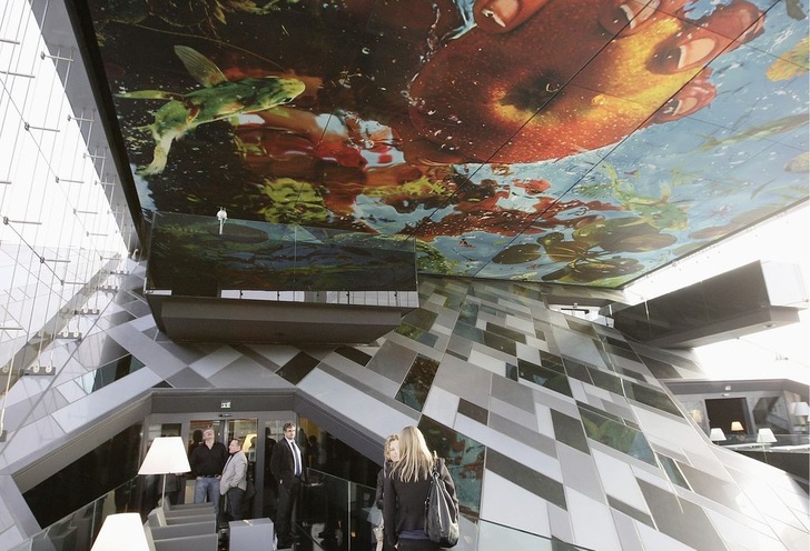 Ansprechender Innenraum des Hotelturms: Die von der Künstlerin Pipilotti Rist gestaltete Lichtdecke des großen, westseitigen Wintergartens wird von einer ­kaleidoskop­artigen Verglasung bis auf den Boden der Hotellobby ­gespiegelt.