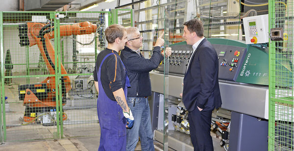 
Achim Haag (r.) und seine Kollegen prüfen die Kantenqualität. An der Kantenschleifmaschine (hier eine Bottero Victralux 111 F) unterstützt der orange Roboter den Bearbeiter, indem der Roboterarm die Glasscheibe vor dem Schleifen jeweils dreht. 
