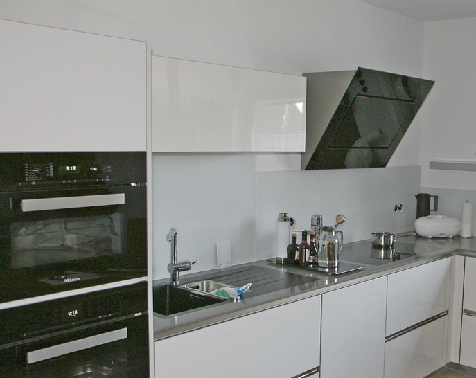 Unter den Küchenschränken mit ihren weißen Glastüren sollten farblich passende Scheiben als Wandverkleidung angebracht werden. Die Wandgläser sind hingegen deutlich dunkler als die Türblenden.