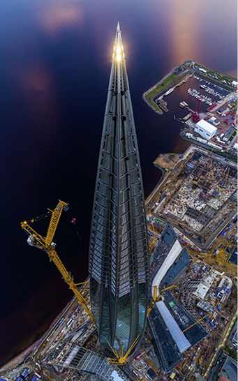 



Das Lakhta Center in St. Petersburg bot zur Fußball-Weltmeisterschaft einen spektakulären Blick auf das benachbarte WM-Stadion. Mit 462 m ist es der höchste Wolkenkratzer Europas. Kurz vor Beginn der Fußball-WM haben die Monteure des Fassadenbauers Gartner, unterstützt von angeseilten Alpinisten, in über 300 Meter Höhe die letzten rund 3 mal 4 m großen Glasscheiben eingebaut. Insgesamt umfasst die gebogene Fassade eine Fläche von rund 14 Fußballfeldern – größer als die Spielflächen aller russischen WM-Stadien zusammen. Im Unterschied zu den übrigen vorgefertigten Fassadenelementen mussten diese Glasscheiben von außen in den gebogenen Aluminiumrahmen gepresst werden. 
