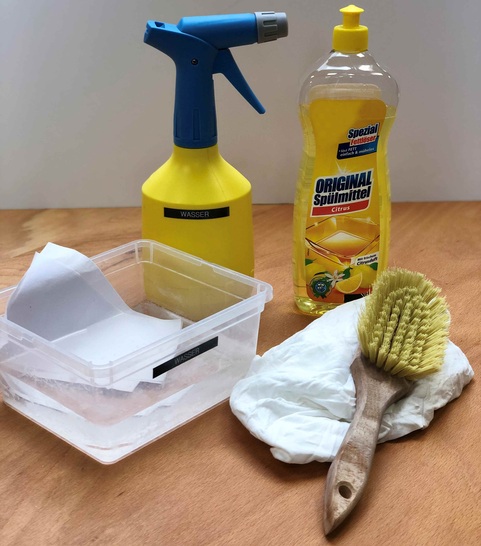 Das passende Equipment, um Folienoberflächen von Verschmutzungen zu befreien: Sprühflasche mit heißem Wasser, Spülmittel, weißes Papier, ein weicher Lappen und eine weiche Bürste.